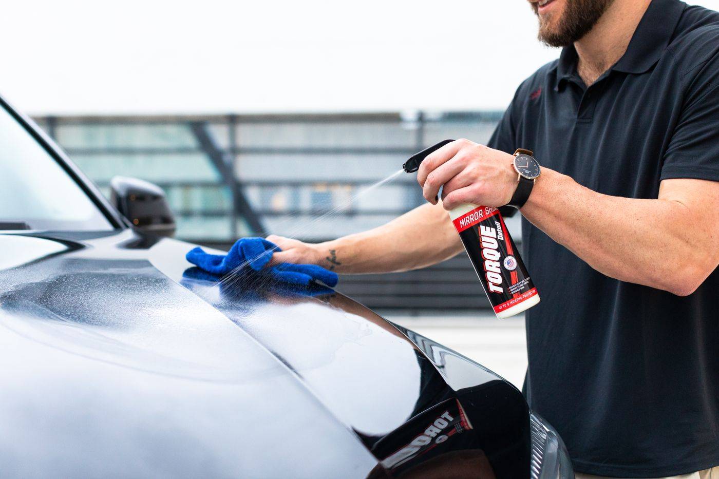A car hood being cleaned with spray and a microfiber cloth outdoors