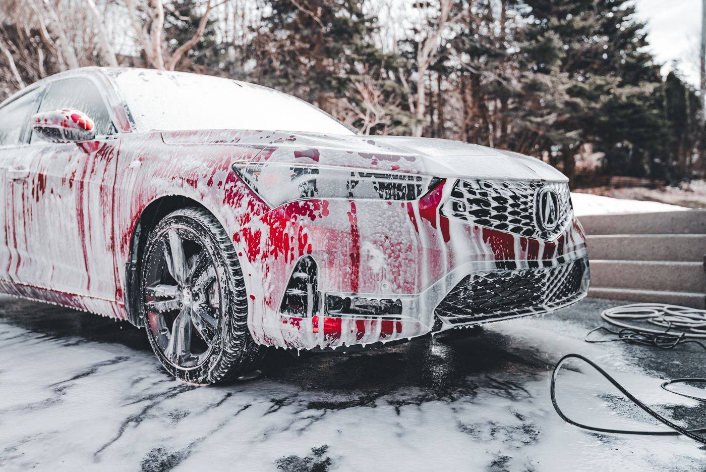 A red car covered in foam during an outdoor hand wash